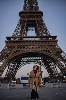 Paris 'teki Eyfel Kulesi' nin arka planında poz veren güzel bir kız. Paris 'te akşam, parıldayan Eyfel Kulesi ve güzel genç bir kadın..