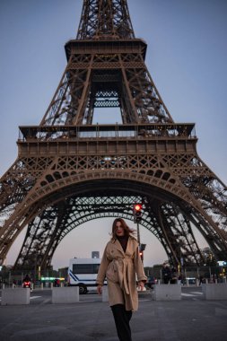 Paris 'teki Eyfel Kulesi' nin arka planında poz veren güzel bir kız. Paris 'te akşam, parıldayan Eyfel Kulesi ve güzel genç bir kadın..