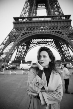 Paris 'teki Eyfel Kulesi' nin arka planında poz veren güzel bir kız. Paris 'te akşam, Parlayan Eyfel Kulesi ve güzel genç bir kadın. Siyah beyaz fotoğraf.
