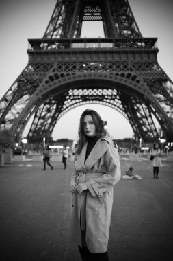 Paris 'teki Eyfel Kulesi' nin arka planında poz veren güzel bir kız. Paris 'te akşam, Parlayan Eyfel Kulesi ve güzel genç bir kadın. Siyah beyaz fotoğraf.