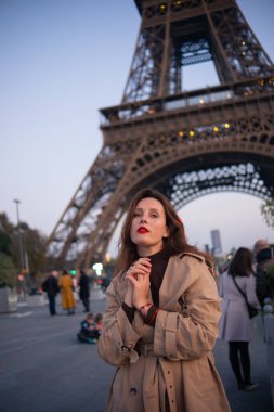 Paris 'teki Eyfel Kulesi' nin arka planında poz veren güzel bir kız. Paris 'te akşam, parıldayan Eyfel Kulesi ve güzel genç bir kadın..