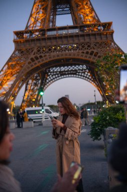 Paris 'teki Eyfel Kulesi' nin arka planında poz veren güzel bir kız. Paris 'te akşam, parıldayan Eyfel Kulesi ve güzel genç bir kadın..