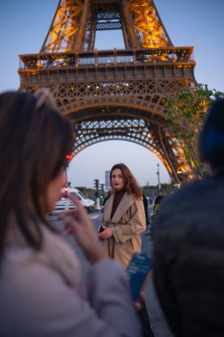 Paris 'teki Eyfel Kulesi' nin arka planında poz veren güzel bir kız. Paris 'te akşam, parıldayan Eyfel Kulesi ve güzel genç bir kadın..