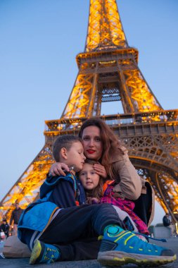 Genç anne, akşam Paris 'te Eyfel Kulesi yakınlarında çocuklarıyla poz veriyor. Paris 'te aile tatili. Eyfel Kulesi 'nin yanında aile yürüyüşü.