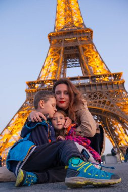 Genç anne, akşam Paris 'te Eyfel Kulesi yakınlarında çocuklarıyla poz veriyor. Paris 'te aile tatili. Eyfel Kulesi 'nin yanında aile yürüyüşü.
