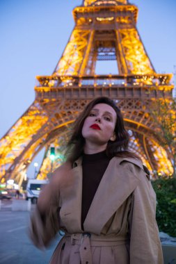 Paris 'teki Eyfel Kulesi' nin arka planında poz veren güzel bir kız. Paris 'te akşam, parıldayan Eyfel Kulesi ve güzel genç bir kadın..