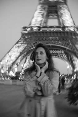 Paris 'teki Eyfel Kulesi' nin arka planında poz veren güzel bir kız. Paris 'te akşam, Parlayan Eyfel Kulesi ve güzel genç bir kadın. Siyah beyaz fotoğraf. Bulanık kavramsal fotoğraf.