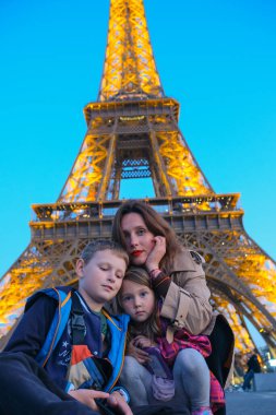 Genç anne, akşam Paris 'te Eyfel Kulesi yakınlarında çocuklarıyla poz veriyor. Paris 'te aile tatili. Eyfel Kulesi 'nin yanında aile yürüyüşü.