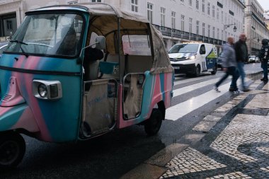 07.02.2025 - Lizbon, Portekiz: Arka planda hareketli Lizbon şehir merkezi olan bir kadın tarafından yönetilen bir tuk-tuk. Sokaklar geçen arabalar, yayalar ve yol boyunca uzanan yüksek binalarla dolu..