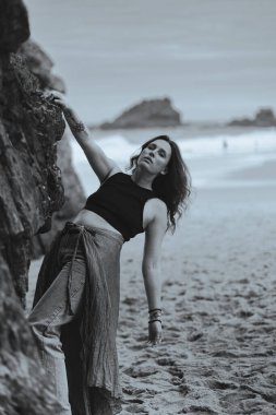 Hint tarzı kırmızı etekli güzel bir kadın okyanus kıyısında kayaların yanında poz veriyor. Sahilde pareo giymiş şık bir kız, şık ve şık bir sanat fotoğrafçısı. Siyah ve beyaz resim.