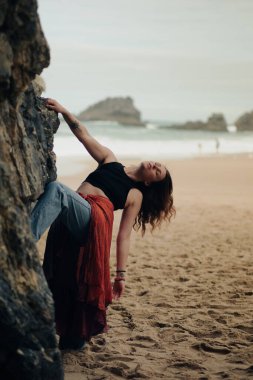 Hint tarzı kırmızı etekli güzel bir kadın okyanus kıyısında kayaların yanında poz veriyor. Sahilde pareo giymiş şık bir kız, şık ve şık bir sanat fotoğrafçısı..