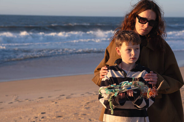 Мальчик и его мать держат большую кучу пластиковых отходов, собранных на пляже. Молодая женщина держит различные пластиковые отходы, выброшенные океаном на пляже.