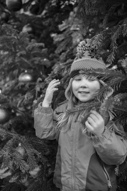 Beş yaşında, kışlık ceketli ve yeni yıl ağacının yanında şapka takan bir kız. Yeni yılda bir kızın portresi.