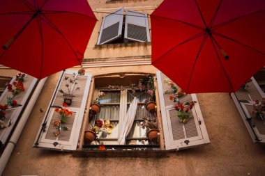 Güzel dekore edilmiş eski bir evin penceresi. Açık panjurlu pencere ve eski bir kasabanın caddesini süsleyen kırmızı şemsiyeler arasında güzel bir dekor..