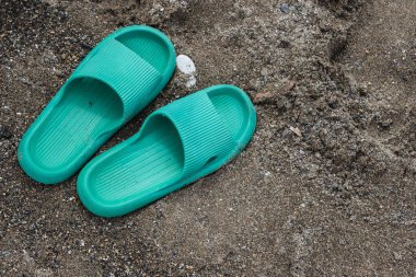 Yeşil yazılar kumun üzerinde duruyor. Lastik terlikler yerde, onların yanında duruyor..