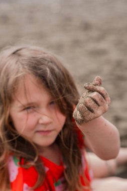Kırmızı tişörtlü güzel kız kameraya bakıyor, işaret parmağı ve başparmağı olan kalp şeklini gösteriyor. Parmaklarla kalp hareketi.