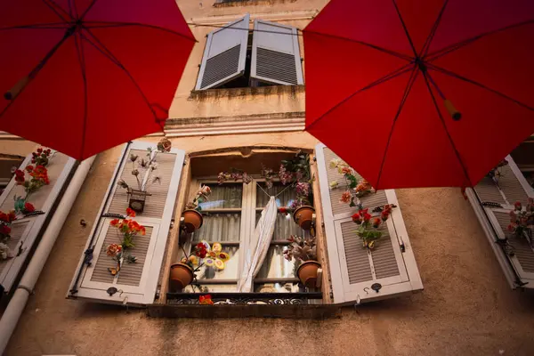 Güzel dekore edilmiş eski bir evin penceresi. Açık panjurlu pencere ve eski bir kasabanın caddesini süsleyen kırmızı şemsiyeler arasında güzel bir dekor..