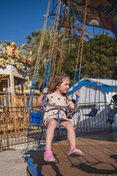 Küçük beyaz bir kız güneşli bir yaz gününde atlıkarıncaya biniyor, gülüyor, el sallıyor ve gezintilerden zevk alıyor. Arka planda palmiye ağaçları yetişir ve diğer sürüşler görülebilir..