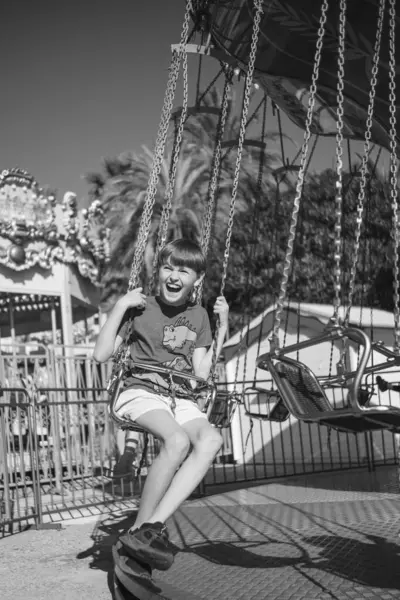 Güneşli bir yaz gününde bir çocuk atlıkarıncaya biniyor, gülüyor, el sallıyor ve eğleniyor. Arka planda palmiye ağaçları yetişir ve diğer sürüşler görülebilir..