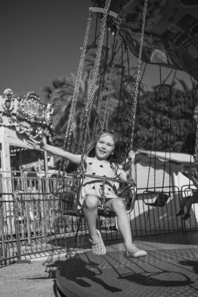 Küçük beyaz bir kız güneşli bir yaz gününde atlıkarıncaya biniyor, gülüyor, el sallıyor ve gezintilerden zevk alıyor. Arka planda palmiye ağaçları yetişir ve diğer sürüşler görülebilir..