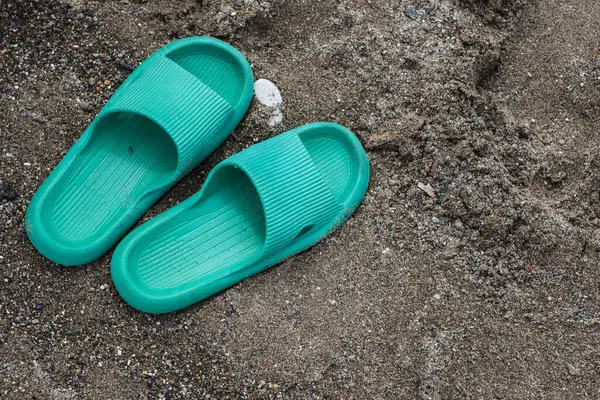 Yeşil yazılar kumun üzerinde duruyor. Lastik terlikler yerde, onların yanında duruyor..