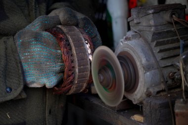 Elektrikli bir motordan bakır bobini öğütme makinesi kullanarak cilalayan bir işçi. Eldivenli eller bir atölyede endüstriyel onarım yapıyor..