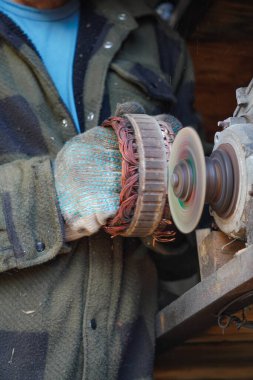 Elektrikli motordan bakır bobini işlemek için öğütme makinesi kullanan eldivenli bir işçi. Endüstriyel onarım ve el işçiliği.
