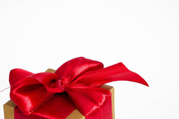 Golden box with red bow and ribbon. Concept of holidays, birthday, Christmas, New Year, Valentines Day and festive decoration on white.