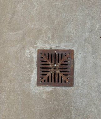 Sert bir beton yüzeyde metal drenaj ızgarası bulunur. Desenli arkaplan gri ve kahverengi tonlarını karıştırarak ızgarayı delik deseniyle renklendirir..