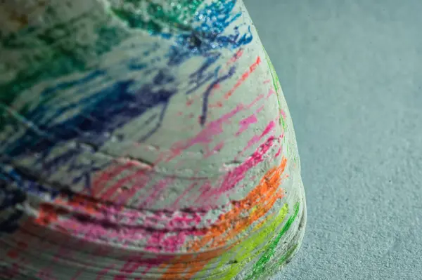 Nahaufnahme einer Muschel mit lebhaften Farbstrichen in Gruen, Blau, Lila, Rosa, Orange und Gelb. Die strukturierte Oberflaeche und kraeftigen Farben schaffen eine creative Verbindung.