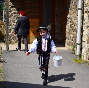 Holloko Paskalya Festivali - Holloko, Macaristan - 18 Nisan 2022 - Çocuk Paskalya yağmuru için bir kova su taşıyor. Geleneksel Paskalya halk kostümü giyip bir Paskalya Festivali 'nde kutlama yapmak.. 