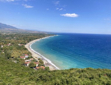 Yunanistan 'da bir Akdeniz, Karayip tarzı kıyı şeridi, sakin bir kumlu sahil, turkuaz deniz ve yemyeşil orman manzarası. Açık mavi gökyüzü, yumuşak dalgalar, uzak dağlar, mükemmel tatil.