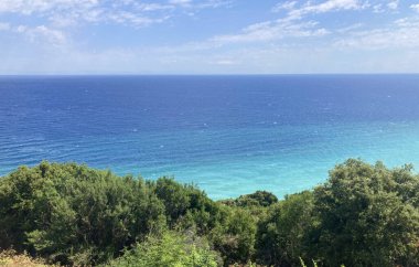 Yunanistan 'da bir Akdeniz, Karayip tarzı kıyı şeridi, sakin bir kumlu sahil, turkuaz deniz ve yemyeşil orman manzarası. Açık mavi gökyüzü, yumuşak dalgalar, uzak dağlar, mükemmel tatil.