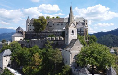 Avusturya Alplerine kurulmuş bir ortaçağ Hochosterwitz kalesi ve kilise kulesinin havadan görünüşü. Taş duvarlar, orman ve dağ manzaralarıyla çevrili bu tarihi kale, Avrupa mimarisi ve kültür mirasına kısa bir bakış sunuyor.. 