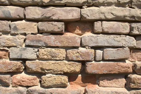 Eski bir tuğla duvara yakın plan, yıpranmış, kırsal doku ve görünür havan topu. Yaşlanmış kırmızı, kahverengi ve kum renkli tuğlalar, arka plan ya da inşaat için uygun kaba yüzey. Klasik duvar, doğal taş ve mimari yapı..