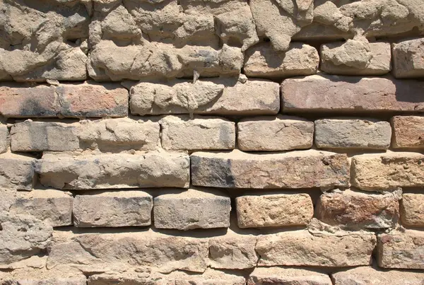 Eski bir tuğla duvara yakın plan, yıpranmış, kırsal doku ve görünür havan topu. Yaşlanmış kırmızı, kahverengi ve kum renkli tuğlalar, arka plan ya da inşaat için uygun kaba yüzey. Klasik duvar, doğal taş ve mimari yapı..