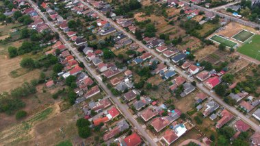Tarlalar, tarlalar ve yeşilliklerle çevrili kırsal bir Macar köyünün manzarası. Dağınık evler, yollar ve insansız hava aracı tarafından yakalanan doğal güzelliklerle dolu huzurlu bir kırsal alan..