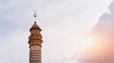Karmaşık desenleri olan tarihi bir minarenin büyüleyici görüntüsü, dramatik bir altın gün batımı gökyüzüne karşı güzel bir şekilde silueti var..