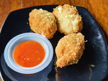 Baharatlı sosla servis edilen üç kızarmış karides peyniri topları, çıtır çıtır ve lezzetli bir dokuya sahip.