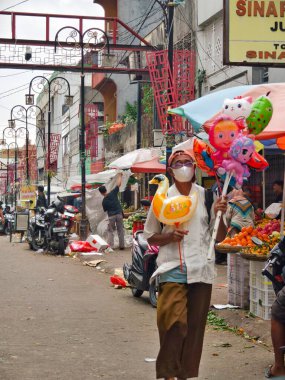 Bogor, Endonezya - 13 Nisan 2025: Endonezya 'da renkli balonlar, taze ürünler ve dinamik aktivitelerle dolu canlı bir Endonezya pazarında balon satıcısı