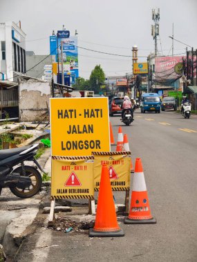 Bogor, Endonezya - 13 Nisan 2025: Endonezya yolu kent manzarasında heyelan ve çukurlar, trafik konileri ve motosikletler için uyarı levhaları ile