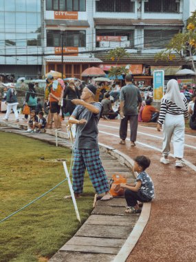 Bogor, Endonezya - 20 Nisan 2025: Büyükbaba torunuyla şehir parkında uçurtma uçuruyor