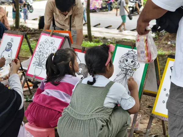 Bogor, Endonezya - 20 Nisan 2025: Çocuklar parktaki bir tuvale, fırça ve suluboya boya kullanarak karakterler çizdiler. Eğitim, ebeveynlik blogları ve yaratıcı içerik için ideal.
