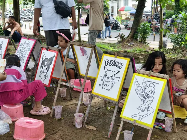 Bogor, Endonezya - 20 Nisan 2025: Parktaki fırça ve boyalarla büyük tuvallere yaratıcı karikatürler çizen enerjik çocuklar, sanat eğitimi ve çocukluk yaratıcılığını vurguladılar. 