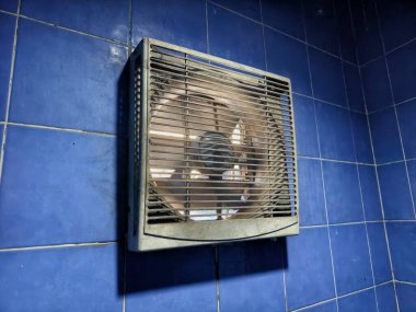 Mavi seramik fayanslar üzerine tozlu duvar monteli egzoz vantilatörü, kapalı alanlardaki ısıyı ve kokuyu azaltmak için kullanılır.