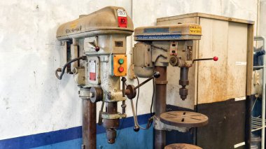 Sabit bir masada metal veya ahşap delmek için kullanılan bir atölyede yan yana duran iki eski bank sondaj makinesi.