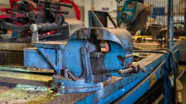 Kesme, delme ya da montaj sırasında nesneleri sıkıca tutmak için kullanılan eski bir mavi metal mengenenin yakın çekimi.