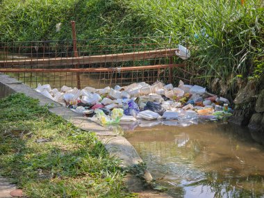 Kirlenmiş bir drenaj kanalı plastik atık ve molozlarla tıkanmış, su kirliliğini ve atıkların uygun olmayan şekilde atılmasını gösteren