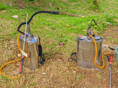 Tarım uygulamalarında kullanılan çimenlerin üzerine portakal hortumları ve başlıkları olan iki metal böcek ilacı spreyi.