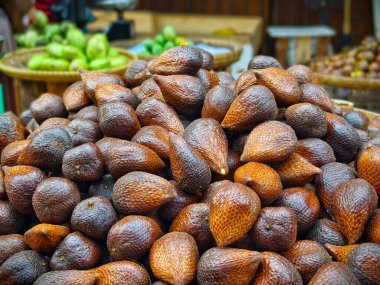 Yerel bir markette kırmızımsı kahverengi derili taze yılan meyvesi yığını, diğer tropikal meyvelerle çevrili.